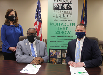 Caucasian male wearing a blue face mask, blue suit jacket, white collared shirt, light blue tie, hands folded while sitting down at a table, white paper in front of him with a green pen; African American male wearing a black Augusta Tech branded face mask, light gray suit, silver Augusta Tech lapel pin, white collared shirt, blue/purple tie, silver watch, hands folded white sitting at a brown table, white papers on brown table in front of him with a green pen; Caucasian female standing wearing a black Augusta Tech branded face mask, blue shirt, hands folded together, black pants, background features an American flag, the state of Georgia flag, large retractable banner showing old Augusta Tech logo, verbiage reads: byl.daves-studio.com, Education That Works; bulleted list reads Allied Health Sciences and Nursing, Business and Personal Services, and Engineering Technology, Industrial Technology, and Learning Support, photos underneath the bulleted list.